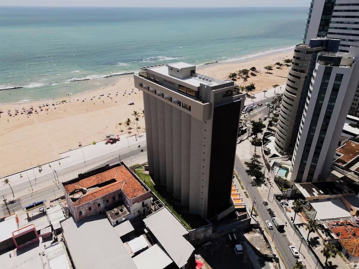 A high-rise hotel with a beach view, a parking lot, and a street with cars.