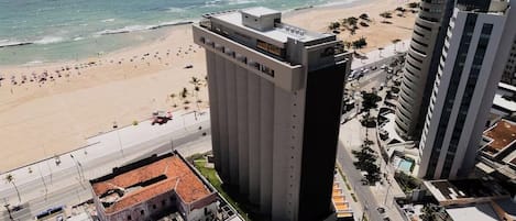 A high-rise hotel with a beach view, a parking lot, and a street with cars.