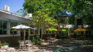 An outdoor patio area with tables and chairs, umbrellas, and potted plants.