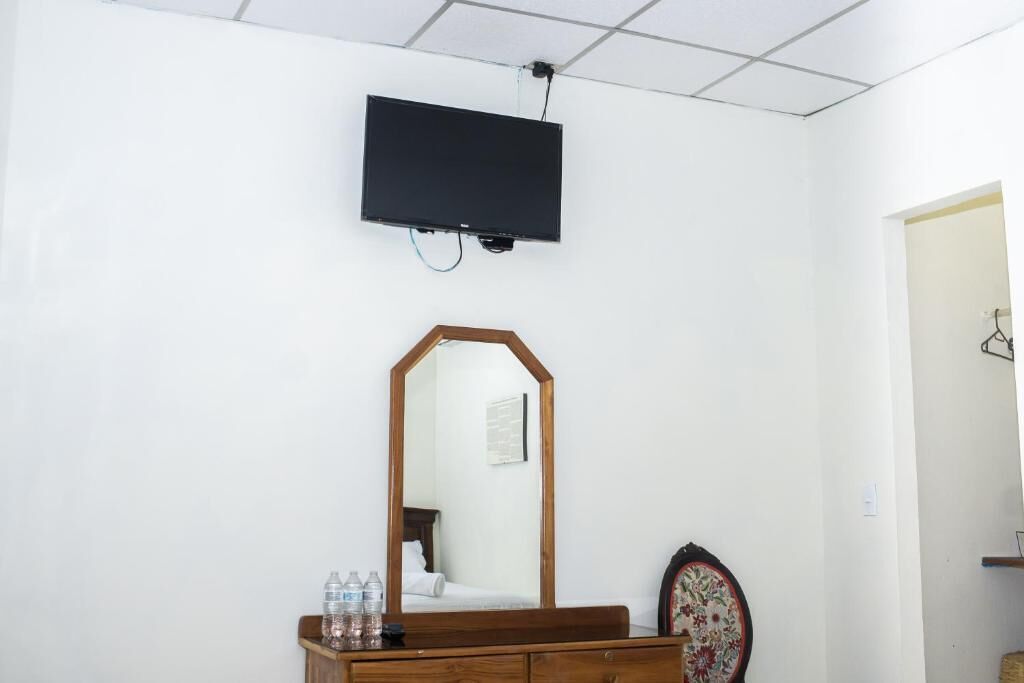 Ein Zimmer mit einem Bett, einer Holzkommode, einem Spiegel, einem an der Wand befestigten Flachbildfernseher und einem gerahmten Bild.