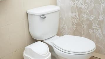 Lavabo amb un safata de brossa a costat, un dispensador de tovallons de paper a la paret i una cortina de bany amb motius florals.
