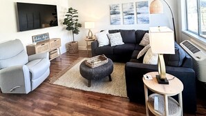 Un soggiorno con ventilatore a soffitto, televisore a schermo piatto, divano, tavolino da caffè e lampada.