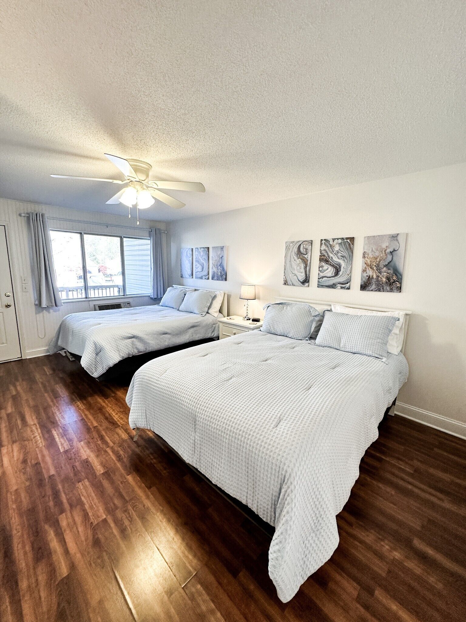 A bedroom with two beds, a ceiling fan, and artwork on the wall.