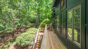 A wooden deck with a bench, a chair, and a large window overlooking a forested area. - Cuesta Verde at Rumbling Bald (Lake Lure)