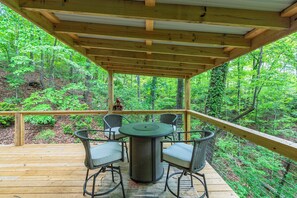 A wooden deck with a round table and four chairs, surrounded by a forest. - Cuesta Verde at Rumbling Bald (Lake Lure)