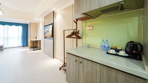 Ein modernes Hotelzimmer mit Küchenzeile, Essbereich und großem Fenster mit Vorhängen.