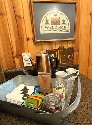 A tray with a coffee maker, a kettle, a jar of sugar, and some tea bags on a kitchen counter.