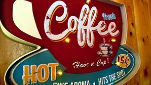 Une enseigne ancienne pour un café, avec les mots « Coffee » (café), « Fresh » (frais), « HOT » (chaud), « Have a Cup » (prenez une tasse) et « 15¢ ».