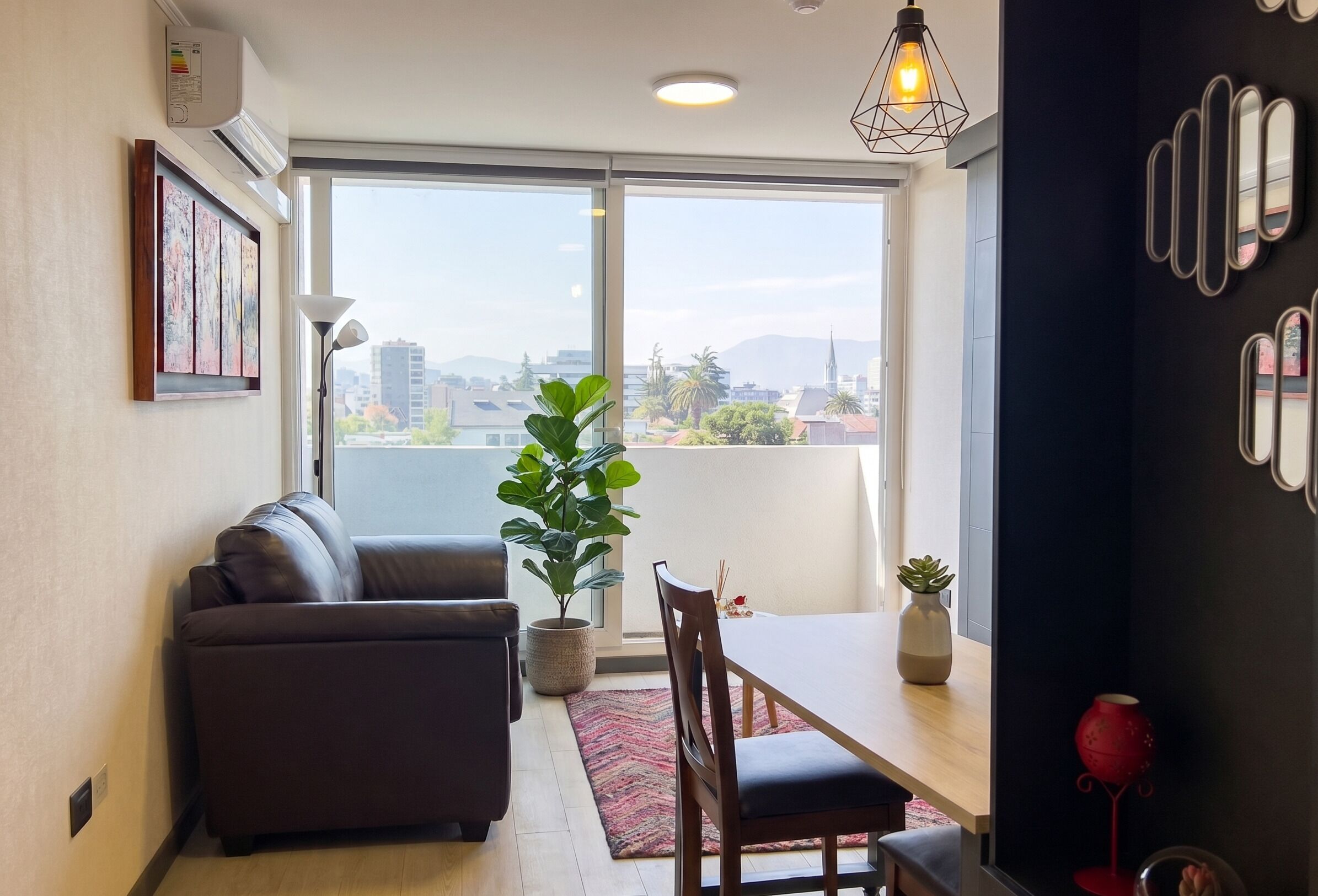 Una sala de estar moderna con sofá, mesa de comedor, sillas, una planta en maceta y vistas amplias a través de ventanas grandes.
