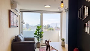 A modern living room with a sofa, dining table, chairs, a potted plant, and a view through large windows. - Centro Cívico - La Moneda - Domus Travels (Santiago)