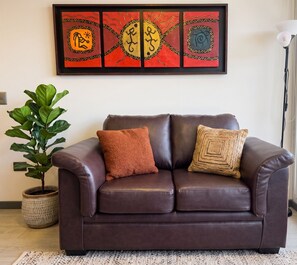 Ein braunes Ledersofa mit zwei Kissen, einer Topfpflanze und einem gerahmten Kunstwerk an der Wand.