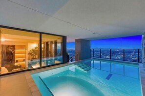 A modern infinity pool with a view of the city at night, a glass-enclosed room with a view, and a staircase leading to the pool area. - Presidential Penthouse Private Infinity Pool (Miami)