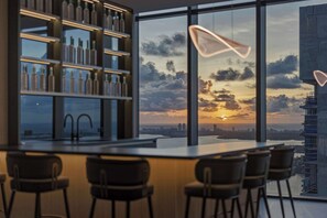 A modern bar area with a city skyline view at sunset, a large window, and a shelf with bottles. - Presidential Penthouse Private Infinity Pool (Miami)