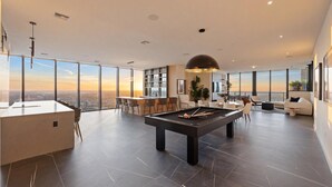 Una sala de estar moderna con mesa de billar, zona de bar y amplias ventanas con vistas a la ciudad.