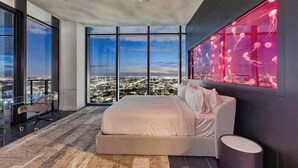 Un dormitorio moderno con una cama grande, un escritorio de vidrio y vistas a la ciudad.