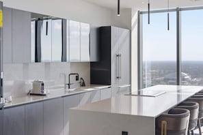 Eine moderne Küche mit einer großen Kochinsel, Edelstahlgeräten und Blick auf die Stadt durch große Fenster.