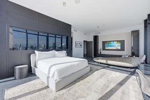 Ein modernes Schlafzimmer mit einem großen Bett, einem Fernseher und Blick auf die Stadt.