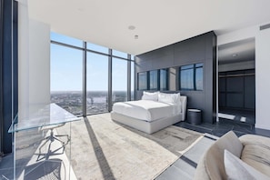 Ein modernes Schlafzimmer mit einem großen Bett, einem Glastisch und Blick auf die Stadt.