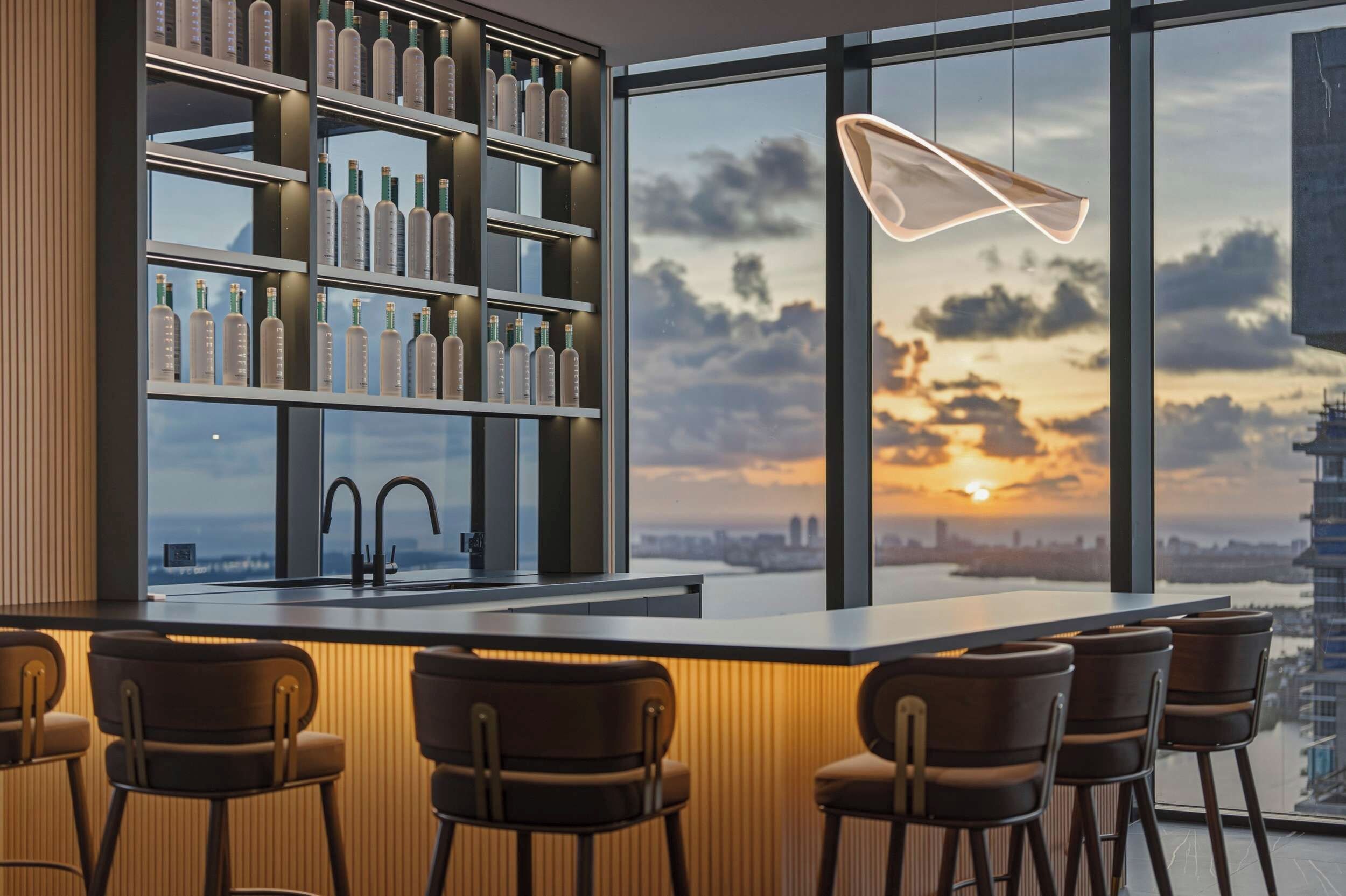 A modern bar area with a city view, bar stools, and a shelf with bottles.