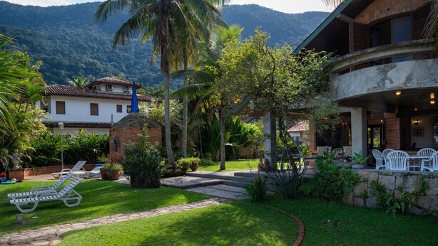A well-maintained garden with a pathway, lounge chairs, and a building with a balcony. - Casa P na Areia com Cen rio Privilegiado Guaec (São Sebastião)