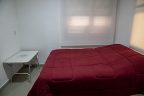 Ein Zimmer mit einem Bett, einem kleinen Tisch und einem Fenster mit Jalousien.