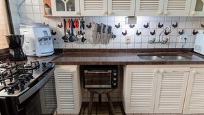 A kitchen with a gas stove, coffee maker, and a toaster oven on a stand. - Casa P na Areia com Cen rio Privilegiado Guaec (São Sebastião)