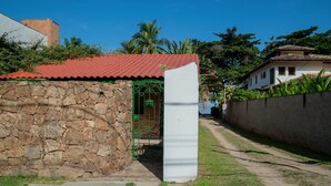 A stone wall, a red-roofed structure, and a white pillar in a garden setting. - Casa P na Areia com Cen rio Privilegiado Guaec (São Sebastião)