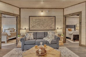 A cozy living room with a grey sofa, a wooden coffee table with a bowl of snacks, and a map on the wall. - Friendly Bear Plunge is a 5br/5ba Vacation Retreat Complete With Beautiful Views (Pigeon Forge)