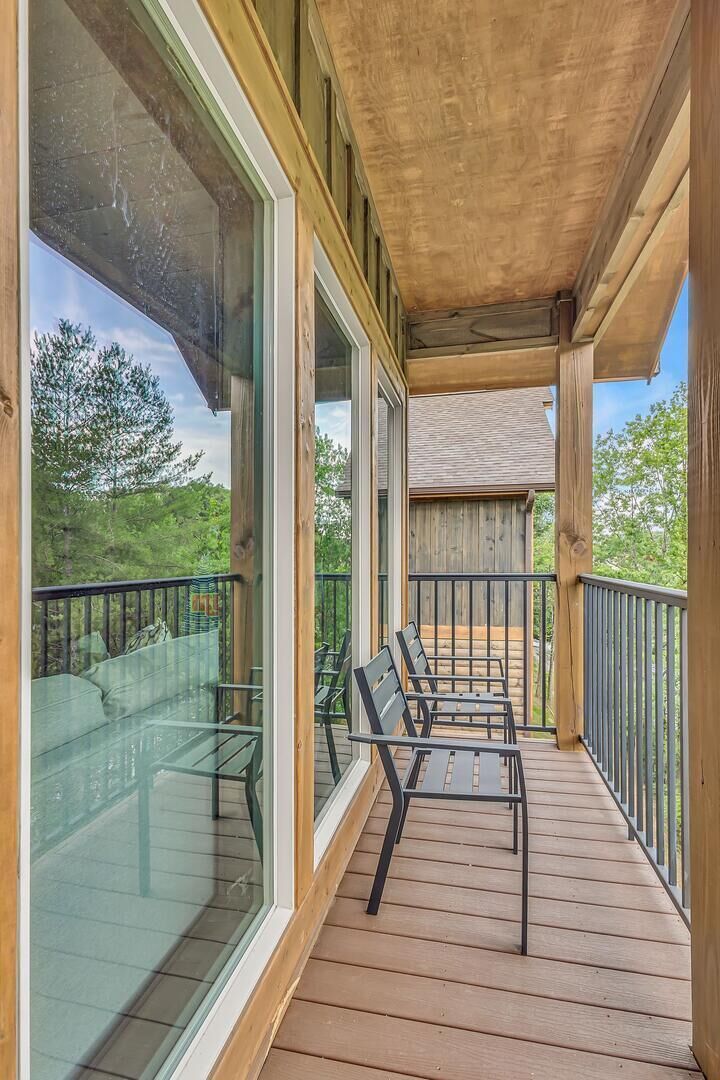 A wooden deck with a glass wall, outdoor seating, and a view of the surrounding landscape.