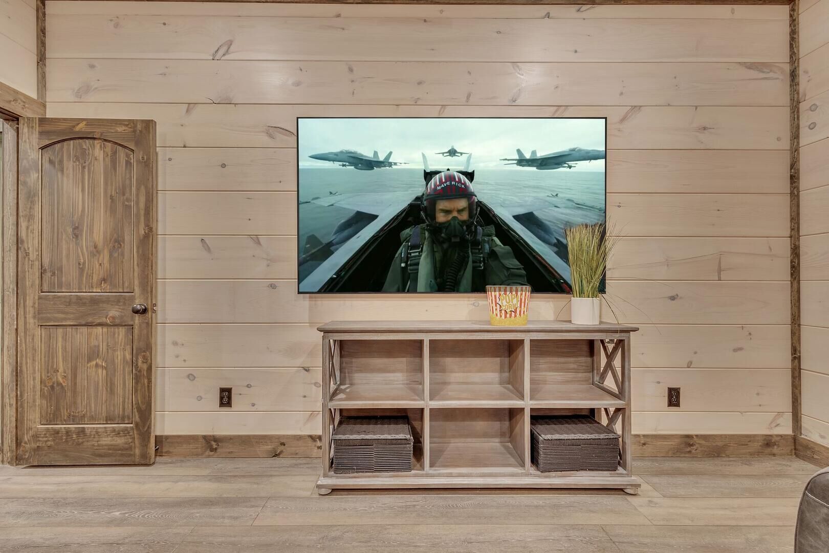 A wooden-paneled room with a television mounted on the wall, a wooden door, and a small table with a popcorn container.