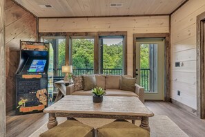 A cozy room with a wooden ceiling, a sofa with cushions, a table with a plant, and a game machine. - Friendly Bear Plunge is a 5br/5ba Vacation Retreat Complete With Beautiful Views (Pigeon Forge)