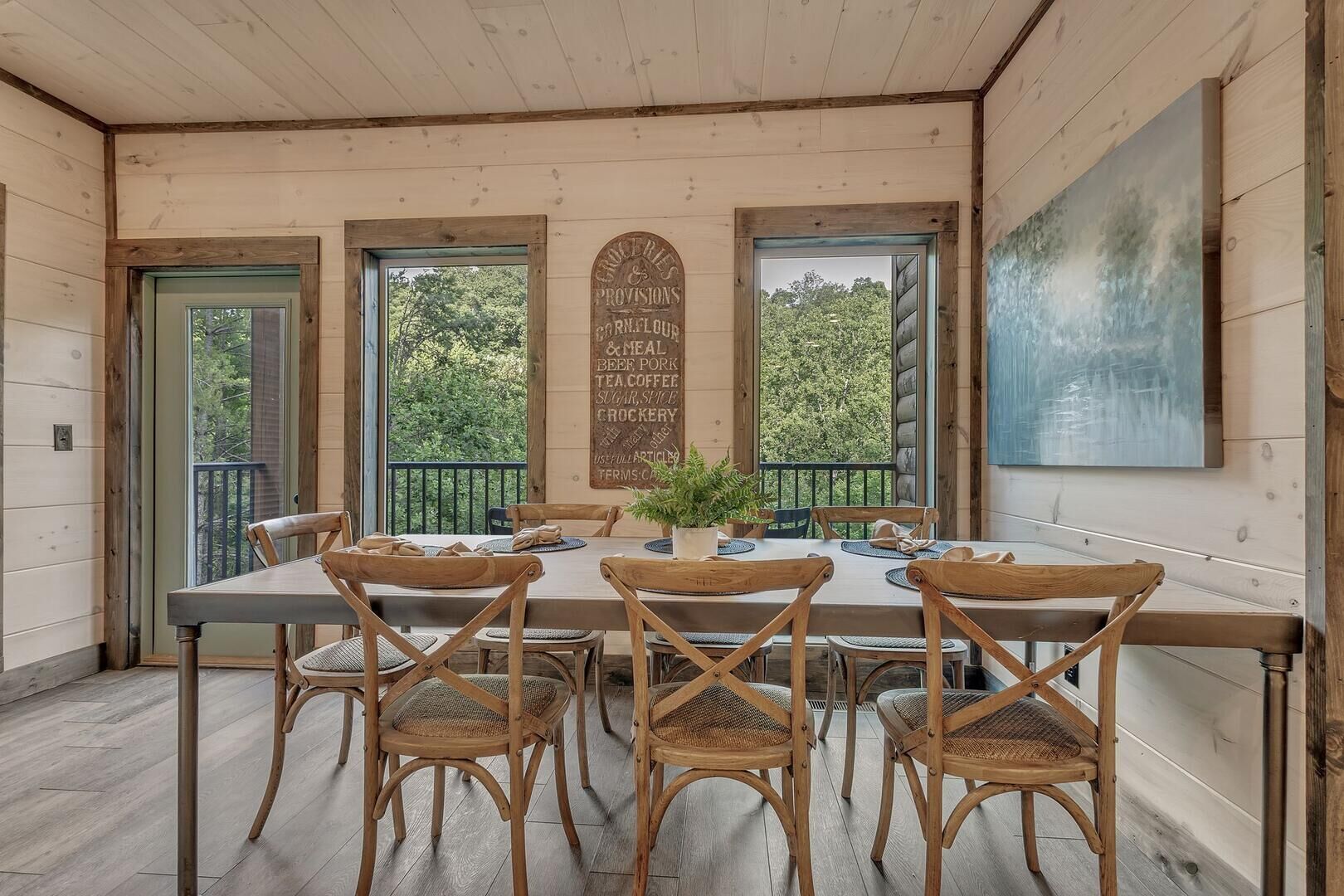A dining area with a wooden table and chairs, a menu board, and large windows with a view of trees.