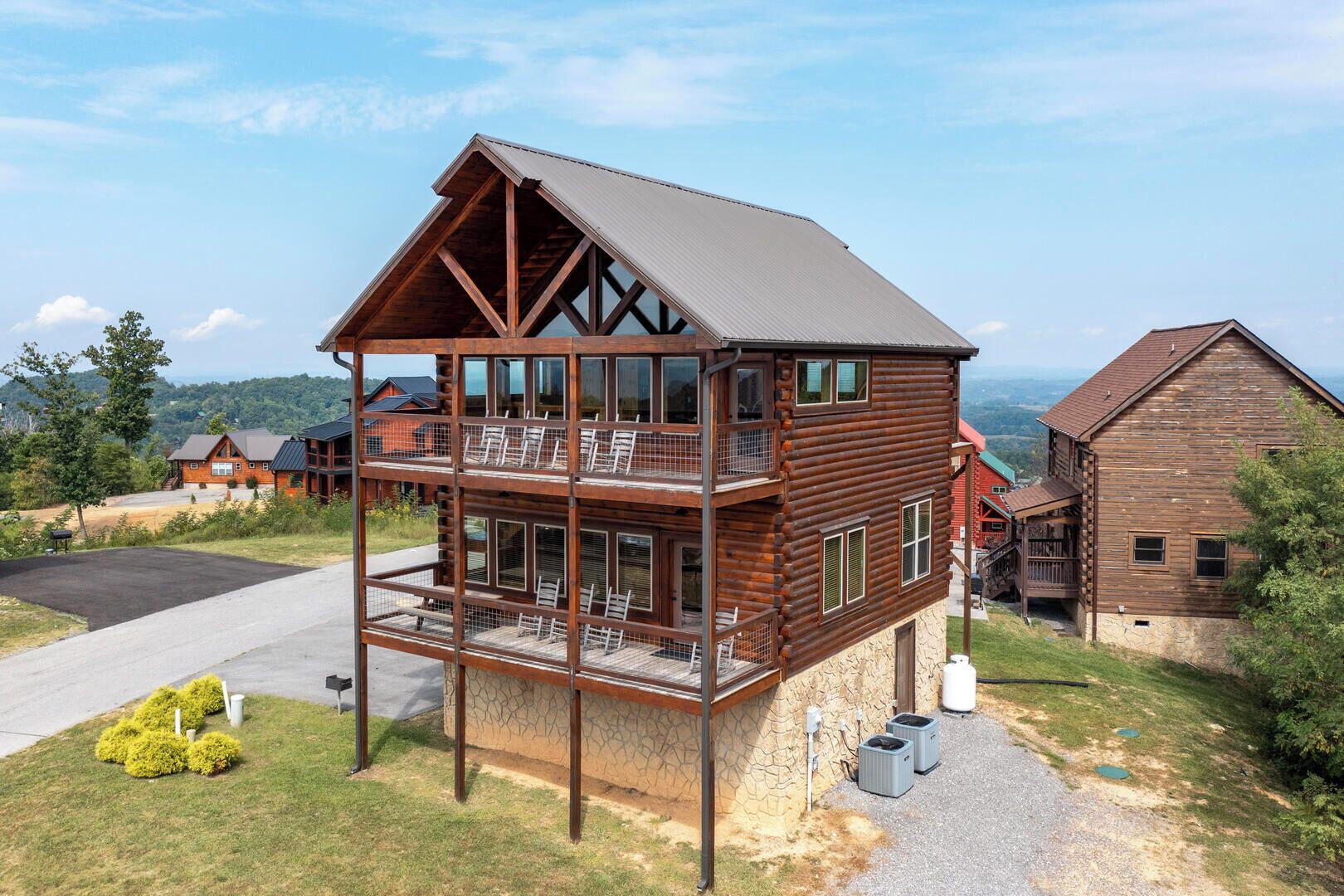 A multi-story log cabin with a balcony, stone foundation, and a view of the surrounding landscape.