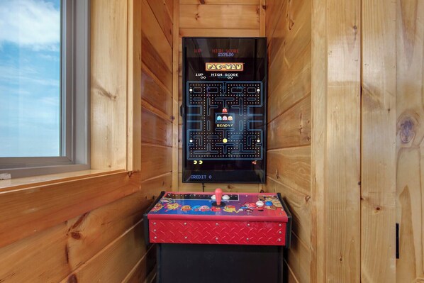 Ein Pac-Man-Spielautomat in einer Holzhütte mit einem Fenster.