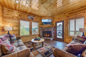 Ein Blockhaus-Interieur mit Kamin, Holzwänden und einer Couch mit gemusterten Kissen.