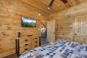 Ein Zimmer mit Holzeinrichtung, inklusive Bett, Kommode, Fernseher und einer Tür zu einem weiteren Raum.