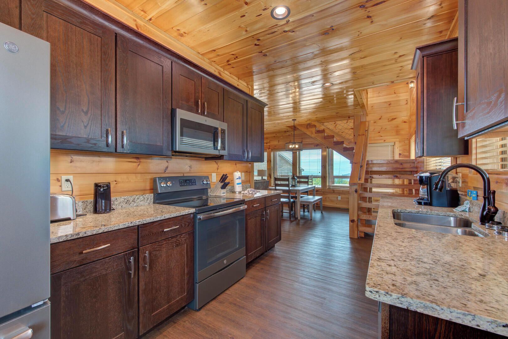 A modern kitchen with dark wooden cabinets, granite countertops, stainless steel appliances, and a dining area with a view.