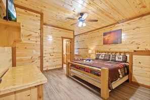 Ein Schlafzimmer einer Holzhütte mit Bett, Deckenventilator und einem Bild an der Wand.