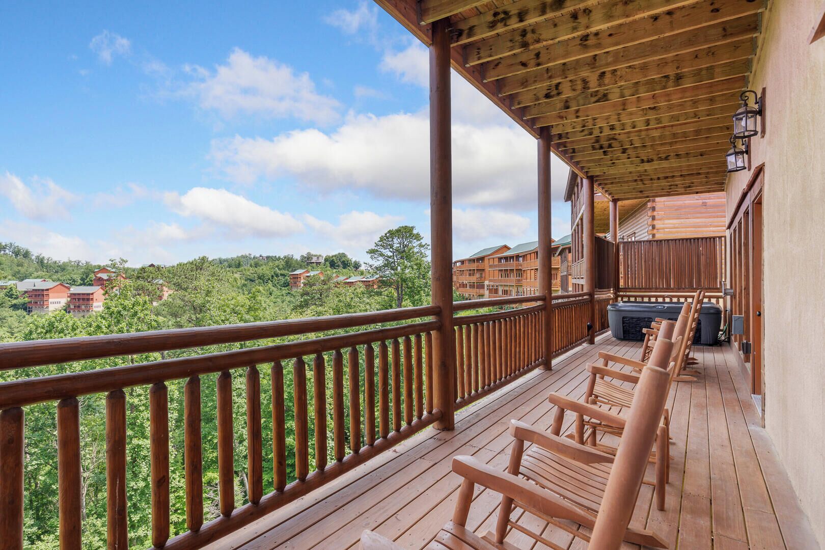 A wooden balcony with a view of a forested area and buildings in the background.
