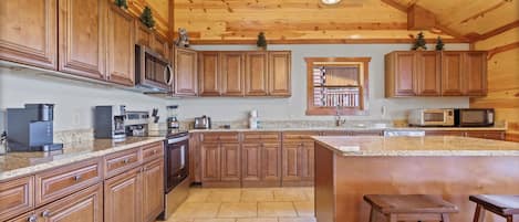 A kitchen with wooden cabinets, granite countertops, a large island, and a hanging light fixture.