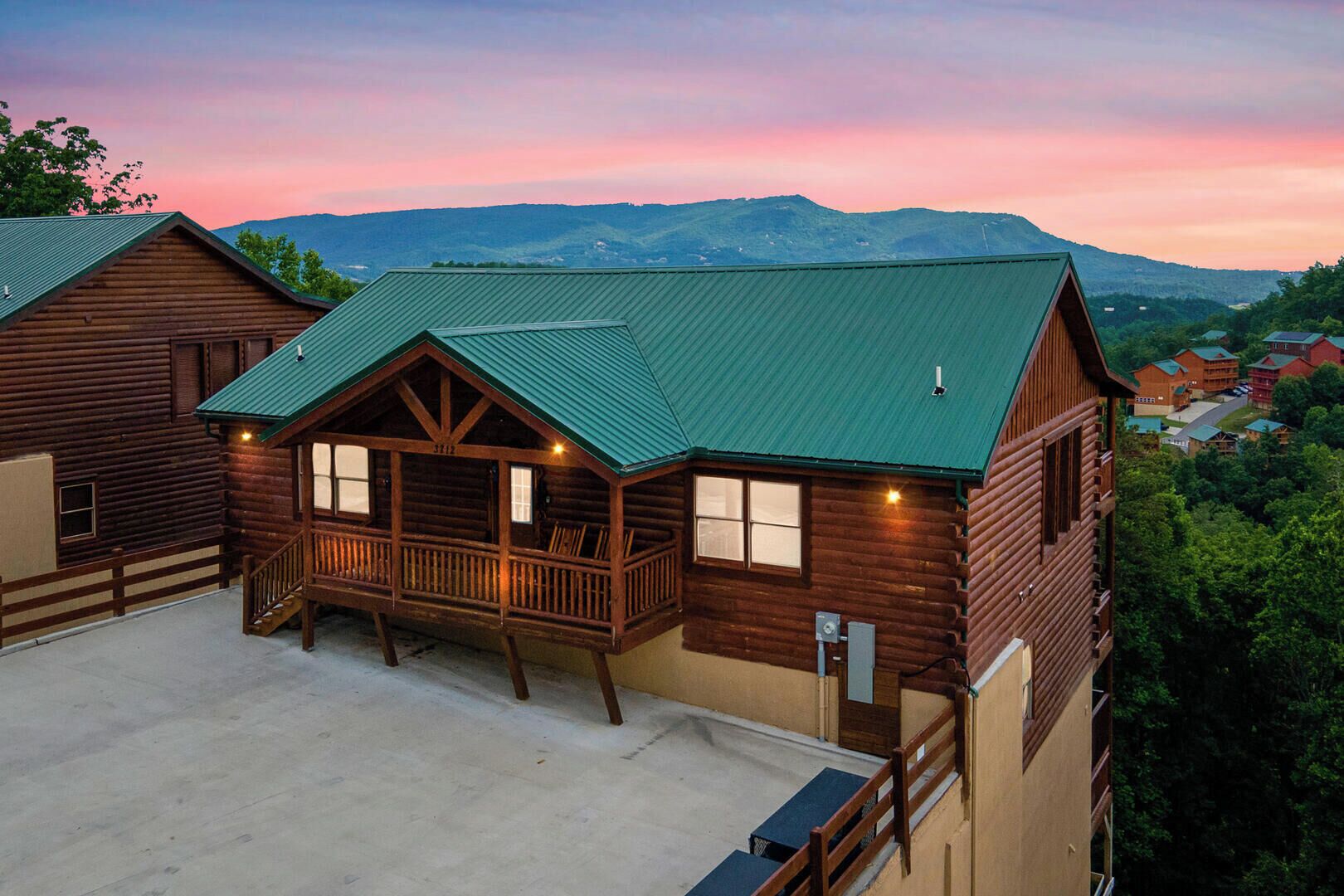 A log cabin with a porch, multiple windows, and a green roof.
