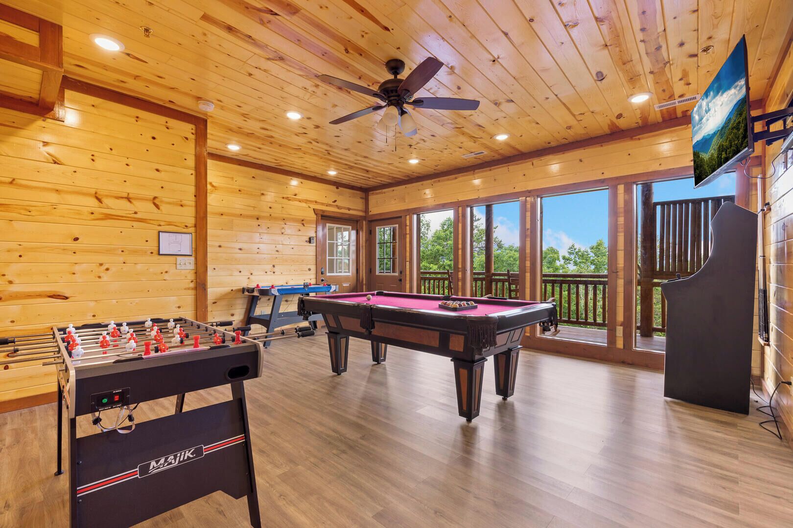 A wooden-floored room with a foosball table, pool table, and a ceiling fan.