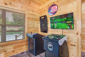Ein Zimmer mit Holzwänden, einem Billardtisch, einer Spielhalle und einem Fernseher, der ein Golfspiel zeigt.