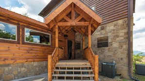 Una baita di legno con rivestimento in pietra, un portico in legno e una scalinata di pietra che conduce all'ingresso.