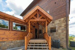 Eine Holzhütte mit einer Steinfassade, einer Holzterrasse und einer Steintreppe, die zum Eingang führt.