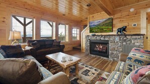 Interno di una baita di legno con camino in pietra, pareti in legno e un'ampia finestra.