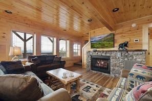 A log cabin interior with a stone fireplace, wooden walls, and a large window. - Amazing View Lodge (Sevierville)