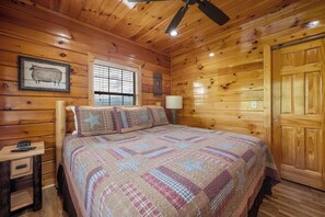 A wooden cabin bedroom with a bed, a nightstand, a lamp, and a ceiling fan. - Amazing View Lodge (Sevierville)