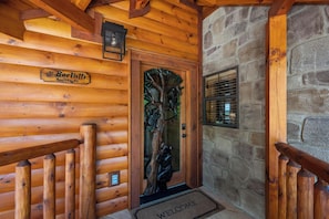 A wooden log cabin entrance with a stone wall, a wooden door with a tree carving, and a welcome mat. - Amazing View Lodge (Sevierville)