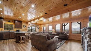 Spazioso interno di una cabina con soffitto in legno, angolo cottura, zona soggiorno con divani e ampie finestre che offrono viste panoramiche.